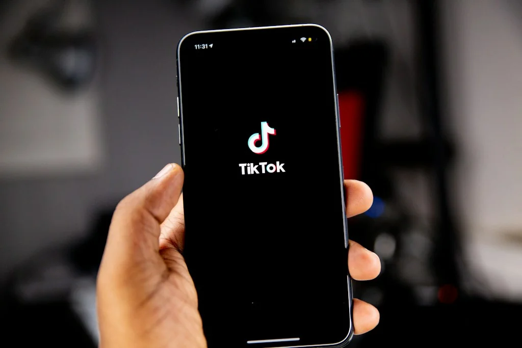 Dłoń trzyma smartfon z logo TikToka na czarnym ekranie.