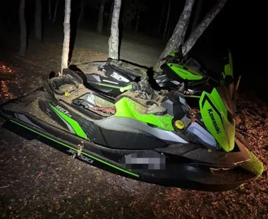 Zniszczony skuter wodny Kawasaki leży w nocy na lesistej, błotnistej ziemi między drzewami.