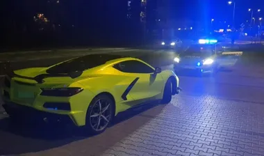 Żółty sportowy samochód osobowy zatrzymany na brukowanej jezdni nocą, obok stoi policyjny radiowóz z włączonymi niebieskimi światłami.