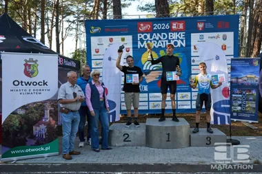Trzech mężczyzn stoi na podium podczas dekoracji laureatów Poland Bike Marathon w Otwocku, a obok nich stoją trzy osoby.